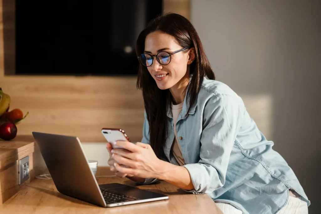 Woman using a smartphone at a desk next to a laptop